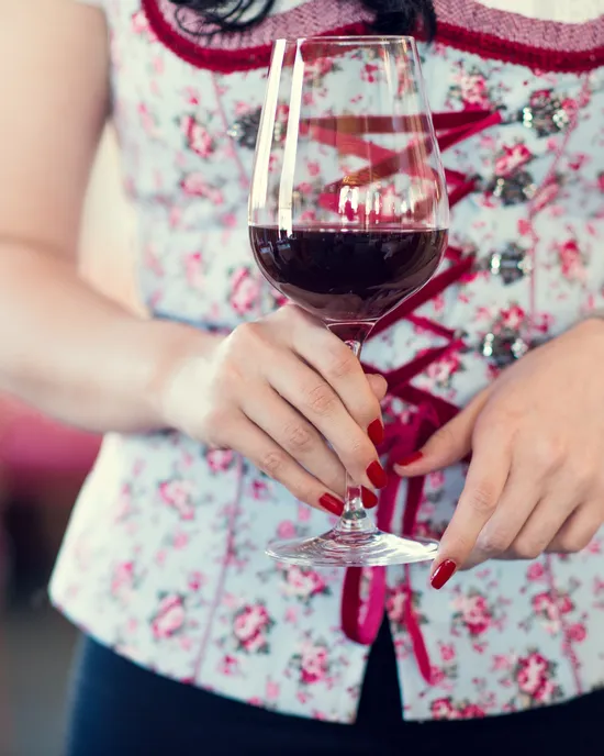 Frau im Blumen-Dirndl hält ein Glas Rotwein auf traditionellem Fest